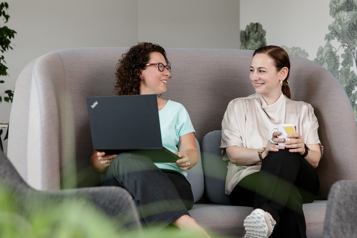 Zwei Beschäftigte Frauen der BAnst PT im freundlichen Gespräch. Es wird gemeinsam am Laptop gearbeitet .