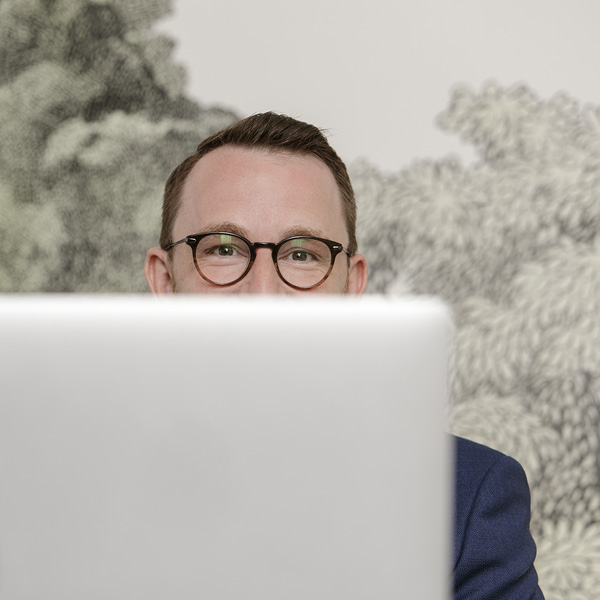 Der Abteilungsleiter, Herr Haag, versteckt seinen Kopf hinter einem Laptop-Bildschirm. Nur die Augenpartie ist noch zu sehen.